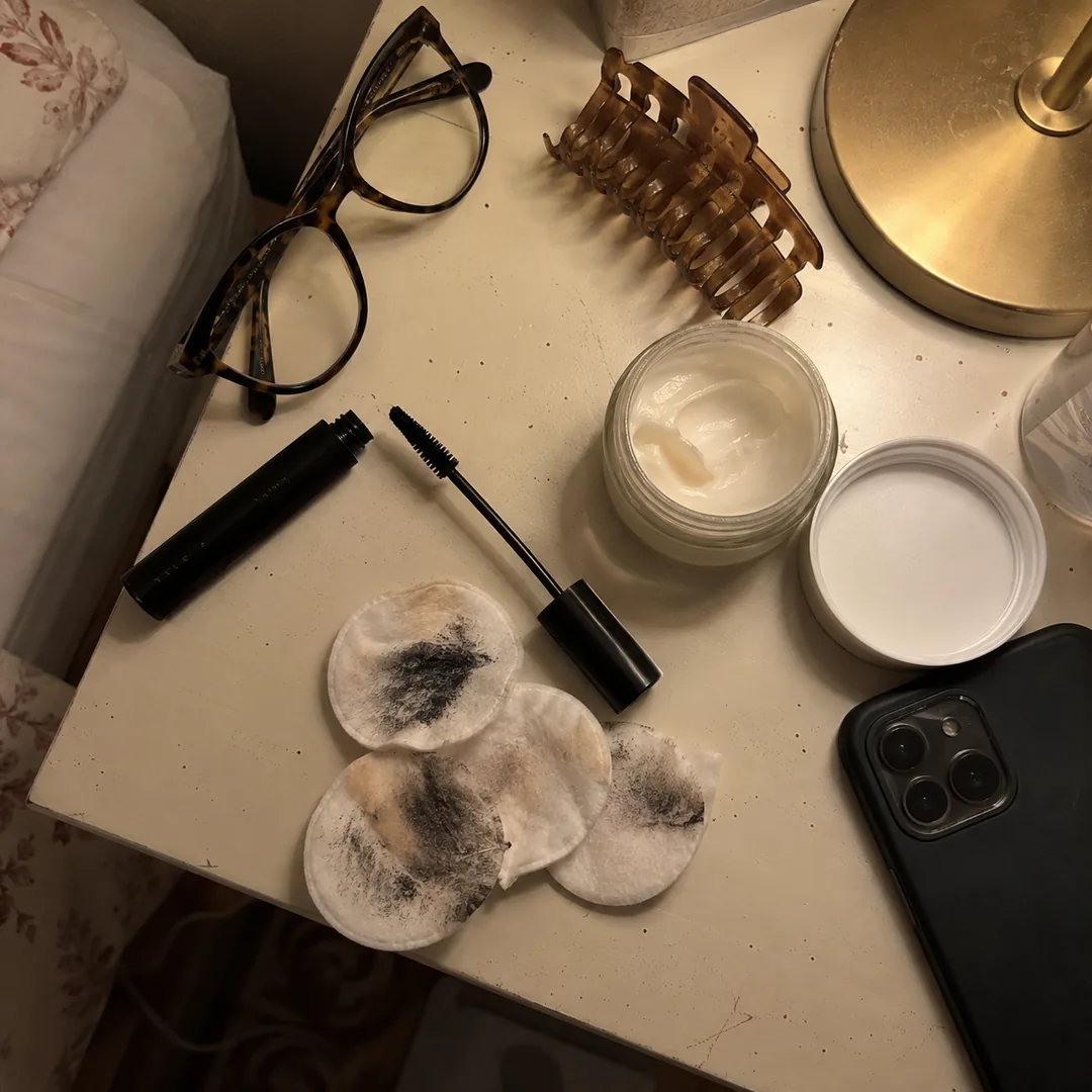 Rímel, crema de noche y algodones con restos de maquillaje en la mesilla
